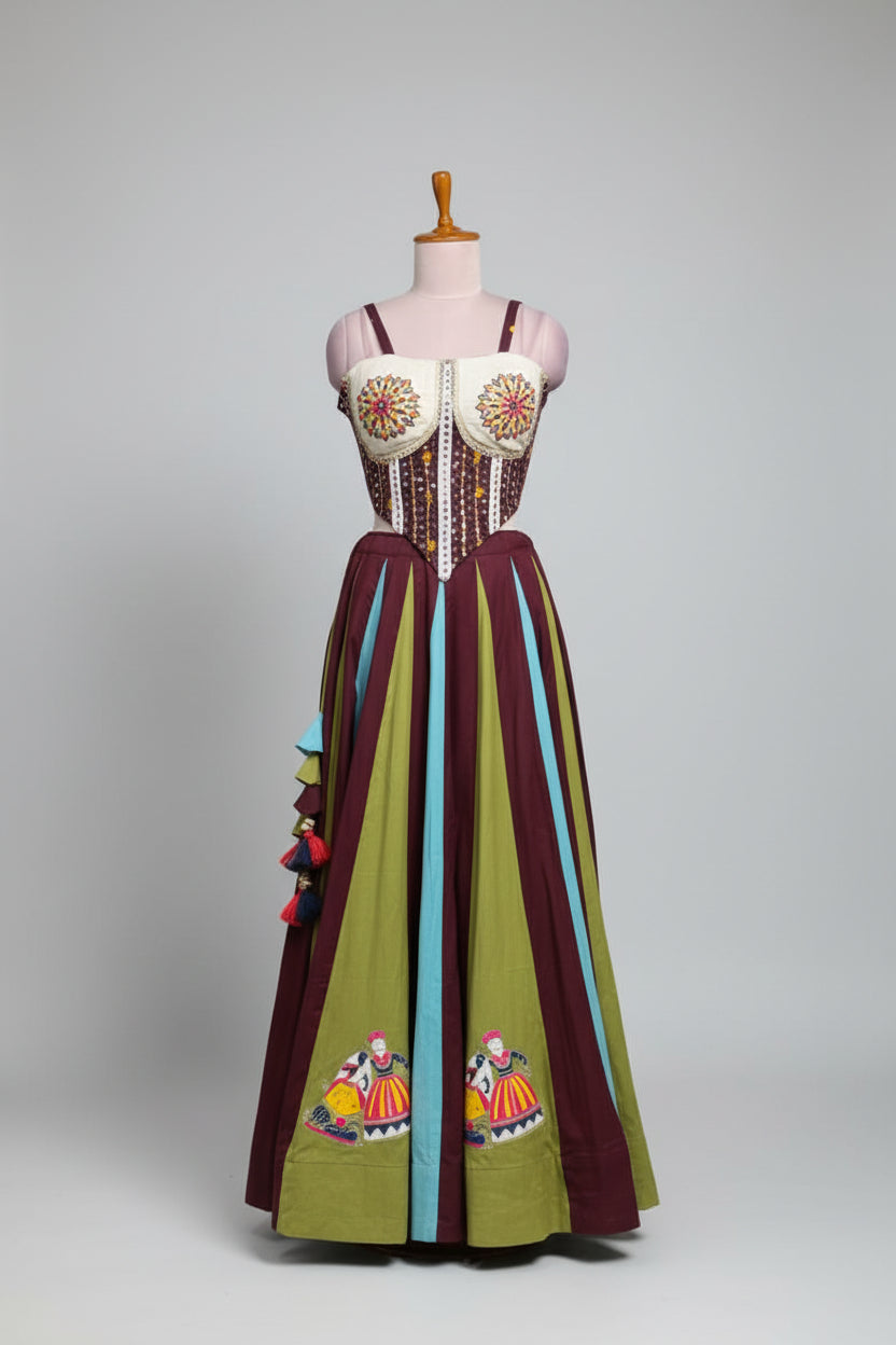 A colorful bohemian-style maxi dress displayed on a mannequin in a clothing store. The dress features a white embroidered bustier top with red and yellow floral patterns, a beaded waist, and a long skirt with vertical stripes of olive green, dark purple, and light blue, decorated with embroidered figures and tassels.