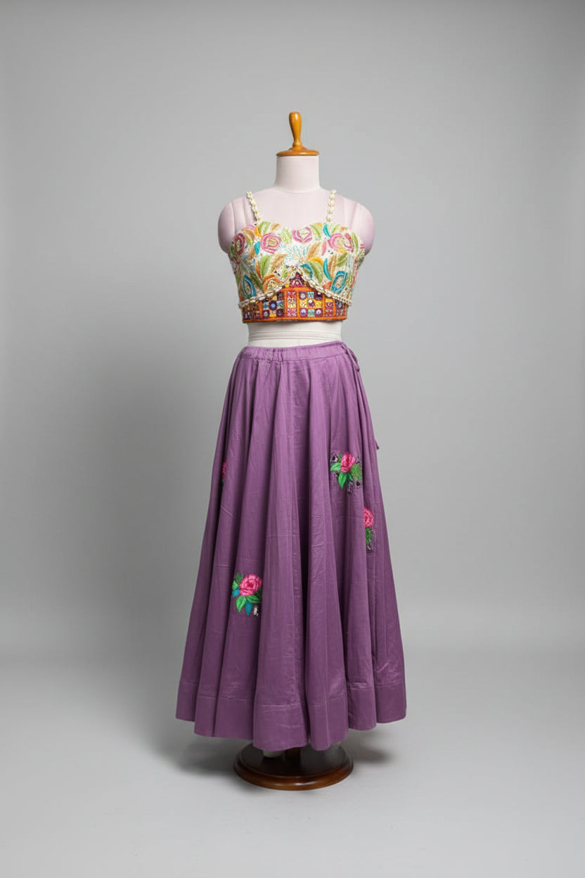 A purple traditional-style skirt with colorful floral embroidery displayed on a mannequin in a clothing store. The outfit includes a matching embroidered sleeveless top, shown against a background of other garments on racks.